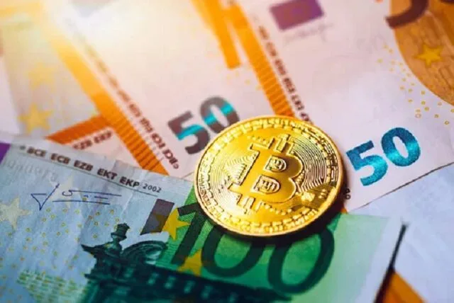 Une pièce dorée à l'effigie du bitcoin posée à côté de billets en euros