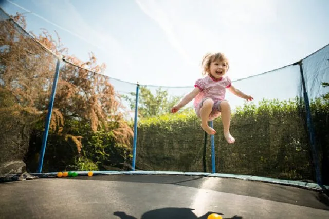 Petite fille sautant seule sur un trampoline de jardin équipé d'un filet