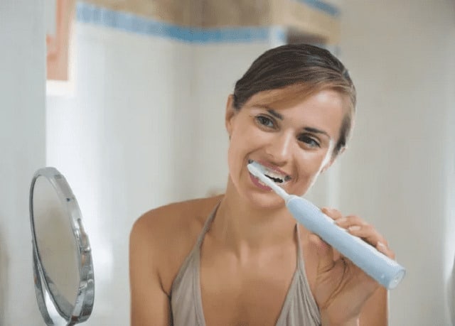 belle dame brossant ses dents avec brosse à dents électrique