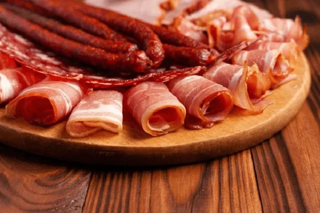 Tranches de charcuterie disposées en rosace sur une planche en bois clair