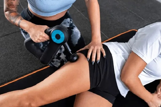 Application d’un pistolet de massage sur le quadriceps, appareil tenu à deux mains