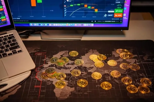 Pièces dorées à l’effigie du bitcoin tenues devant un écran de cotation