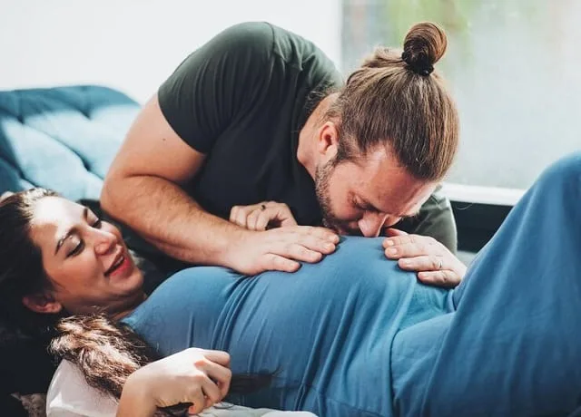 Un couple assis dehors, l'homme posant la main sur le ventre arrondi de sa compagne